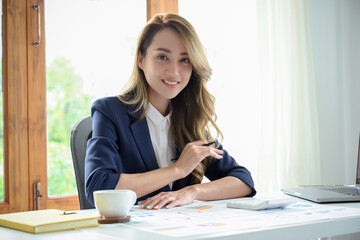 Beautiful Asian businesswoman sits at her office desk with a successful facial expression.