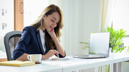 Beautiful Asian businesswoman sits at her office desk, laptop and financial report are on the table.