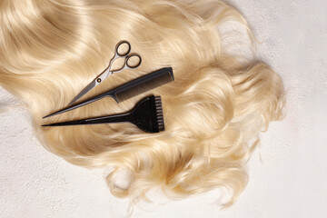 Shiny wavy blonde hair with hair cutting shears and comb on white background, top view