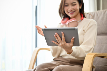 Beautiful Asian female relaxes in the living room using a digital tablet touchpad.