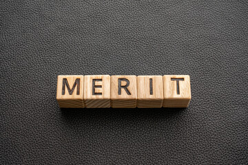 Merit - word from wooden blocks with letters, Merit praise reward concept, black leather background