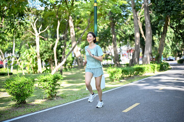 Active young Asian female runner in sportswear running at the beautiful green park