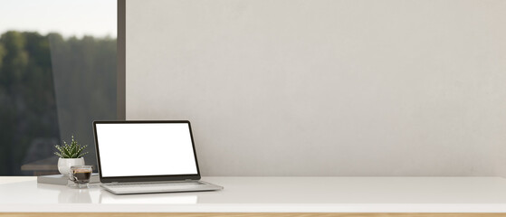 White tabletop workspace with notebook laptop mockup and copy space over white wall.
