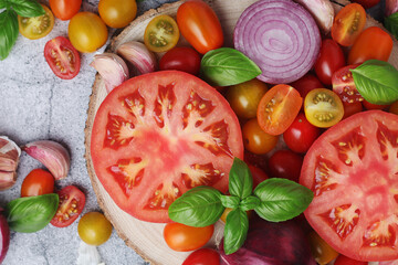 Flat lay composition of different tomatoes, onion, basil and garlic	