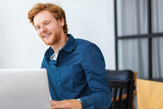 Successful businessman working using computer laptop sitting at the workplace in modern office. Bearded man entrepreneur in shirt typing on keyboard, smiling
