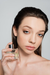 portrait of young woman with blue eyes holding bottle with perfume isolated on grey