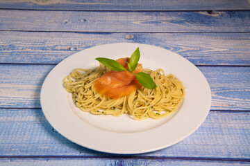 Pasta spaghetti with pesto sauce and fresh basil leaves in white plate, blue background, High quality photo