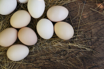 Fresh raw eggs and straw on wooden surface, flat lay