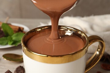 Pouring yummy hot chocolate into cup on table, closeup