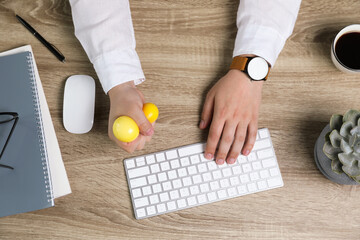 Man squeezing yellow stress ball while typing on computer keyboard at table, top view
