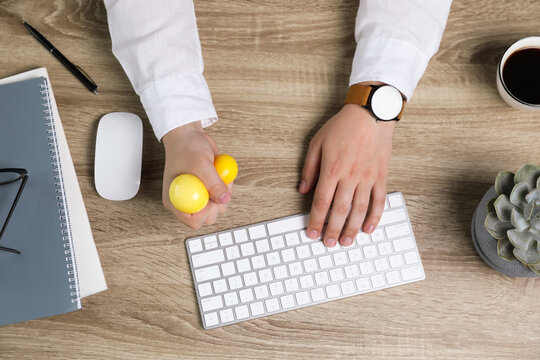 Man Squeezing Yellow Stress Ball While Typing On Computer Keyboard At Table, Top View