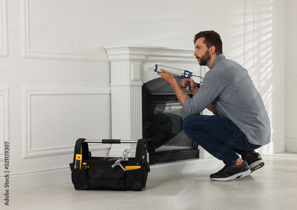 Wall mural Man sealing electric fireplace with caulk near white wall in room