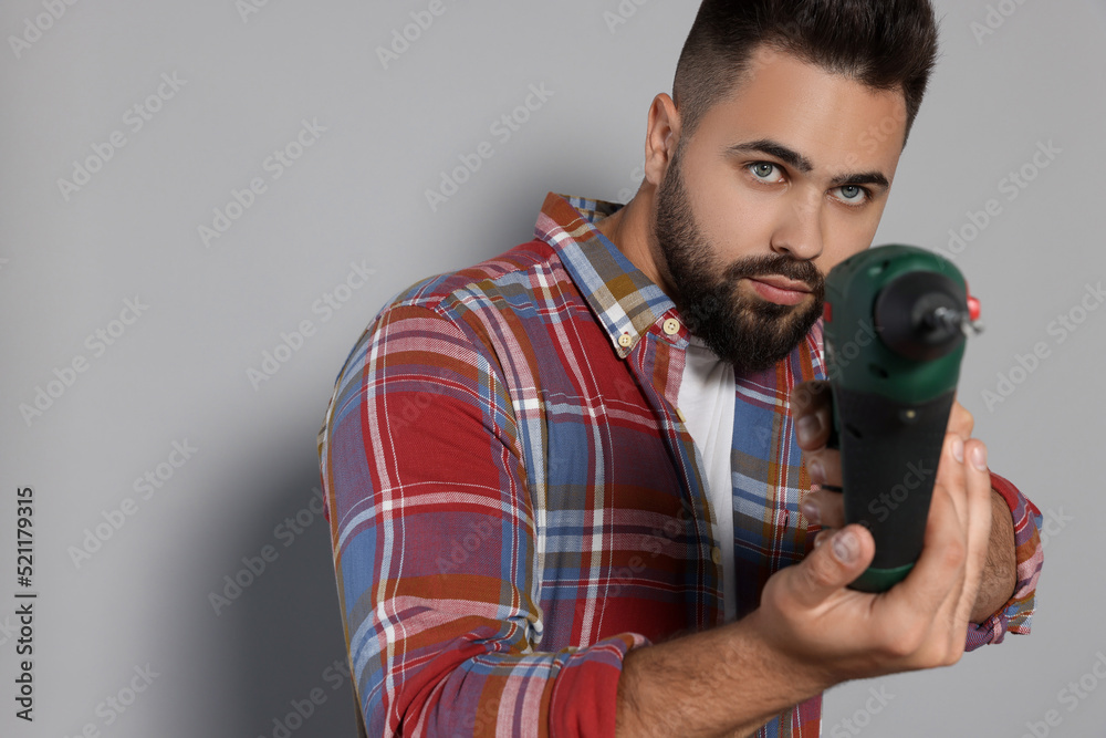 Sticker Young man with power drill on grey background. Space for text