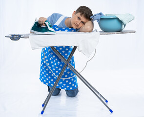 a man in a blue apron, blue t-shirt, jeans and white sneakers with an iron and crumpled linen sits...