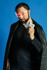 portrait of a man in a studio in a black leather coat. model with a beard on a blue background. trendy luminous glasses on the face