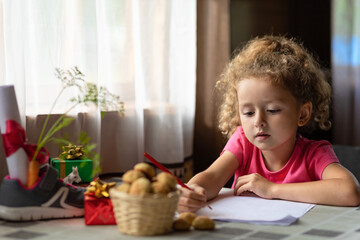 child writing letter on traditional Dutch holiday Sinterklaas in Europe, Netherlands, Belgium. girl put in in boot, shoe carrot for Santa horse, gift, pepernotin chocolate sweet cookies.  soft focus