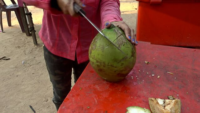Woman openning a young coconut with a big cleaver knife