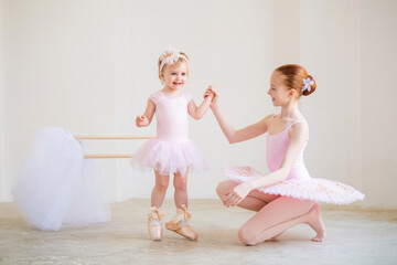 The older sister, a ballerina in a pink tutu and pointe shoes, shows the baby how to practice at...