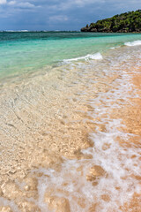 Gentle crystalline wave breaking over the sands along the shore, white foam.