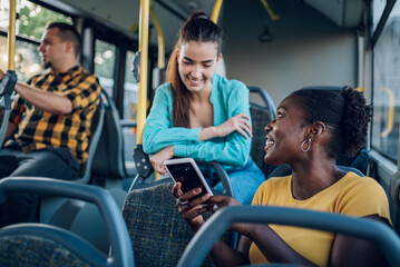 Multiracial group of friends talking while riding in a bus and using a smartphone