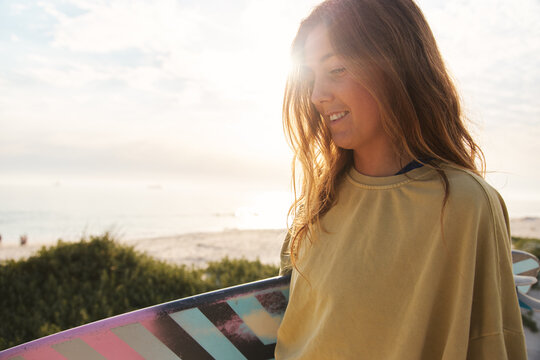 Cropped Shot Of Young Female Adventurer At The Beach Walking Down Sand Dunes With Surf Board Or Kite Surfing Sunset
