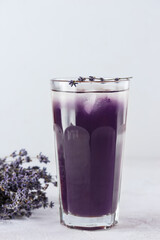 Lavender drink with ice in a glass on a light background.