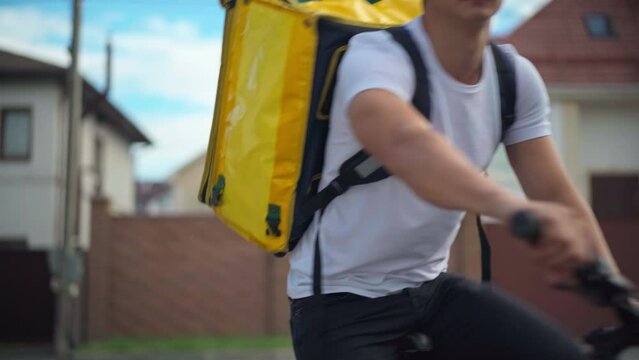 Medium shot portrait of young delivery man raising palm asking for giving way leaving on bike. Caucasian courier delivering food and drink in town outdoors riding away on bicycle
