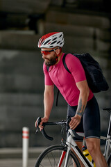 Portrait of a cyclist standing under a bridge with a bicycle in his hand, posing at the camera against an architecture background. Active lifestyle. Cycling is a hobby.