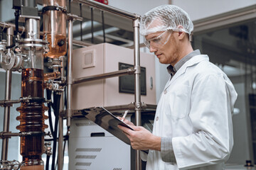 Scientist holding paper board and checking rotational vaporizer during CBD oil extraction, hemp oil...