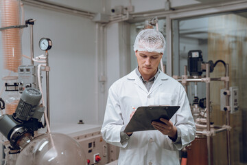 Scientist holding paper board and checking rotational vaporizer during CBD oil extraction, hemp oil extraction process.