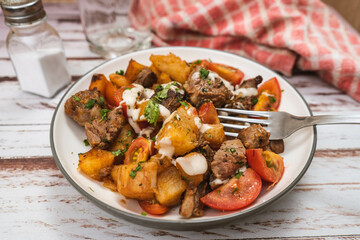 Chunks of meat sauteed with cassava or manioc, chives, pepper, lemon and cherry tomato on a rustic surface. High view.