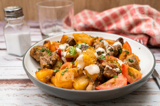 Chunks of meat sauteed with cassava or manioc, chives, pepper, lemon and cherry tomato on a rustic surface. High view.