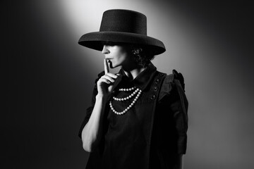 Portrait of beautiful woman in image of famous fashion designer posing in stylish black hat. Black and white photography. Secrets of fashion - obrazy, fototapety, plakaty