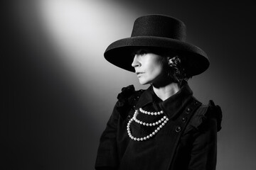 Portrait of beautiful woman in image of famous fashion designer posing in stylish black hat and...