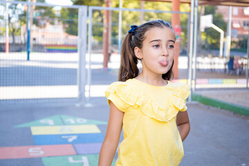 pretty girl in the schoolyard is playing hopscotch while sticking out her tongue as a funny taunt.