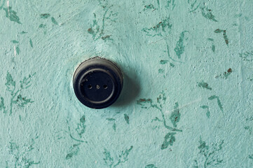 An old electrical outlet hangs on the wall of an abandoned room, a black antique outlet covered...
