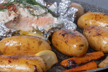 Close-up of appetizing oven baked potatoes and carrots with baked salmon in foil in the background.