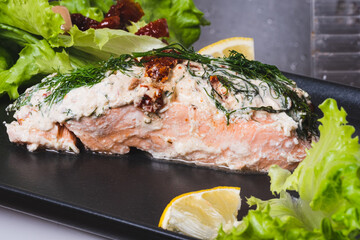 Appetizing oven baked salmon steak with lemons and fresh lettuce served on gray plate.
