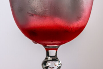 Close-up of dewy glass of refreshing drink with ice cubes on white background.