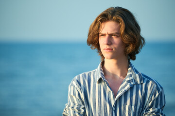 Portrait of serious young teenager boy at sea sunset