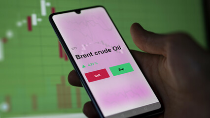 An investor's analyzing the brent crude oil etf fund on a screen. A phone shows the prices of Brent crude Oil