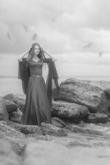 Young medieval maiden on stones by the stormy sea in black and white