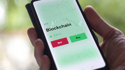 An investor's analyzing the blockchain etf fund on a screen. A phone shows the prices of crypto. 