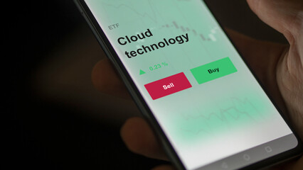 An investor's analyzing the cloud technology etf fund on a screen. A phone shows the prices of CLOUD TECHNOLOGY. 