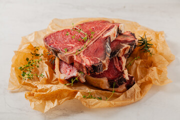 Raw t bone steak, served on paper. Herbs, stone background.