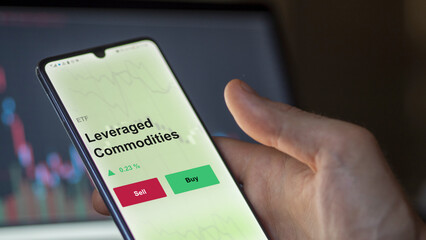 An investor's analyzing the leveraged commodities etf fund on a screen to invest. A phone shows the prices of leverage, leveraged-commodities ETF