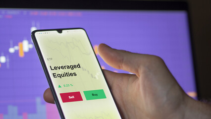An investor's analyzing the leveraged equities etf leverage fund on a screen to invest. A phone shows the prices of leverage, leveraged-equities ETF