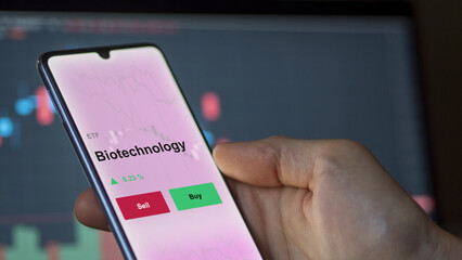 An investor's analyzing the biotechnology etf fund on a screen. A phone shows the prices of bio-technologies ETF to invest blue chips.