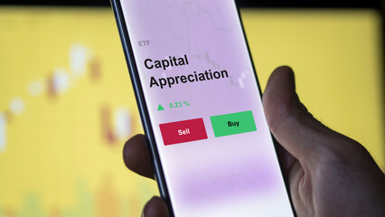 An investor's analyzing the capital appreciation etf fund on a screen. A phone shows the prices of a fund ETF blue chips.