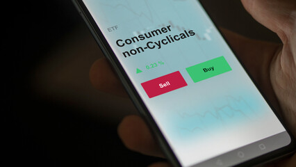 An investor's analyzing the consumer non-cyclicals etf fund on a screen to invest. A phone shows the prices of consumer non cyclical ETF blue chips..